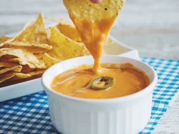 a tortilla chip dipped in vegan nacho cheese