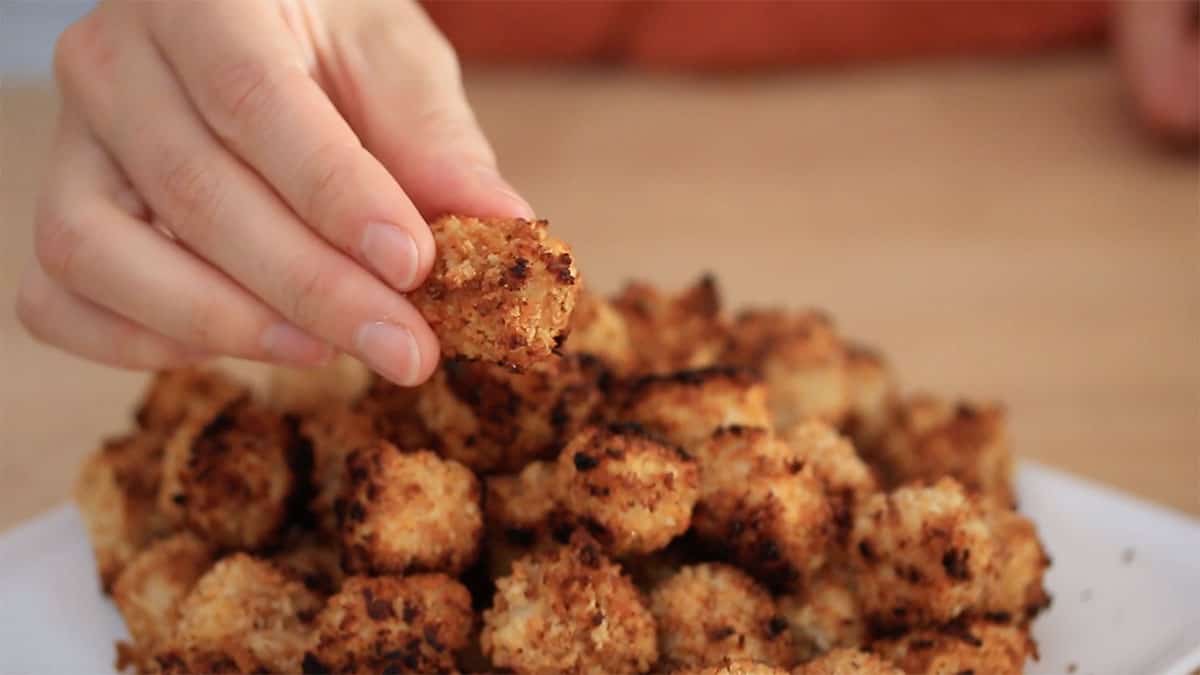 golden brown crispy battered tofu in a pile with a hand holding one piece