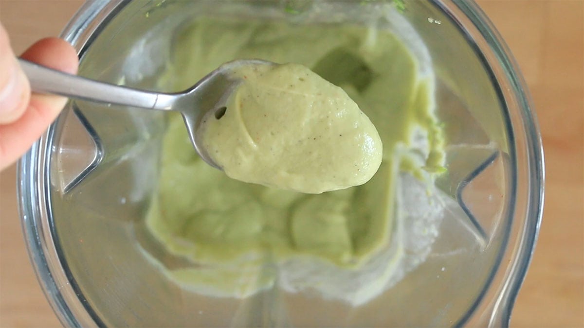a spoon with a scoop of avocado crema over the blender