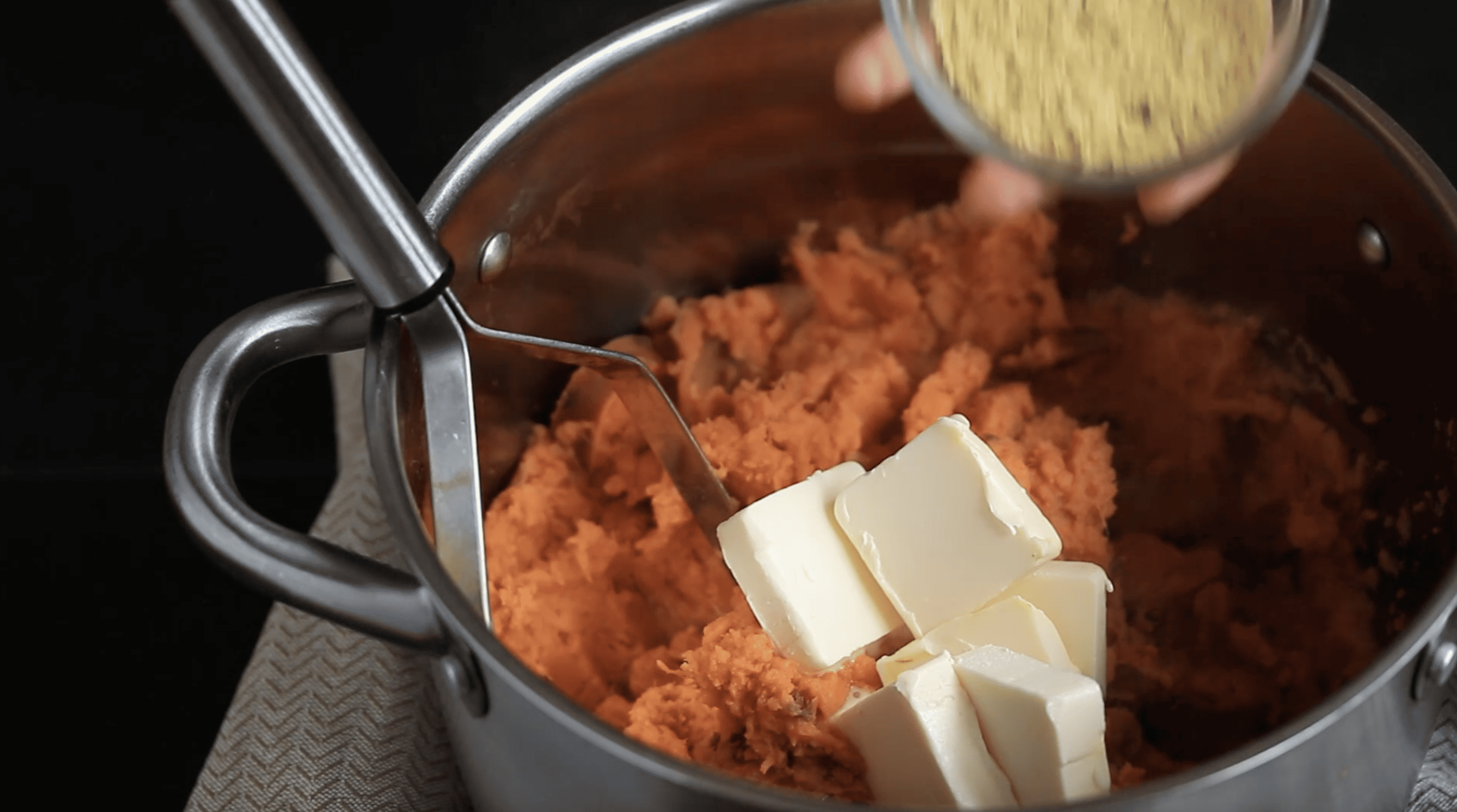 seasonings being added to a pot of sweet potato mash