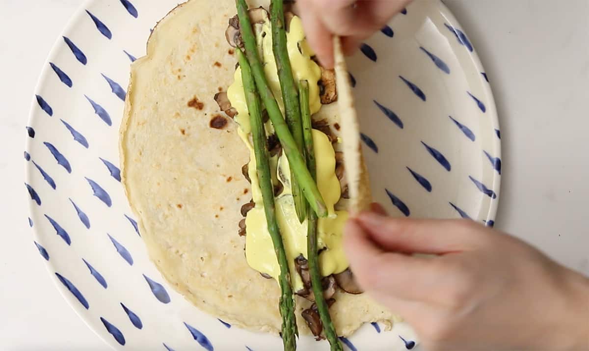 a vegan crepe being rolled with mushrooms and asparagus inside