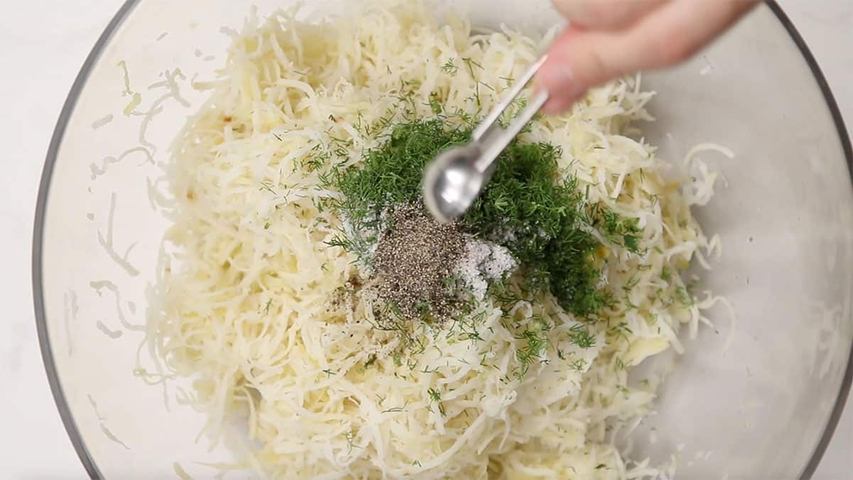 overhead of shredded potato and sauerkraut in a mixing bowl with spices being added