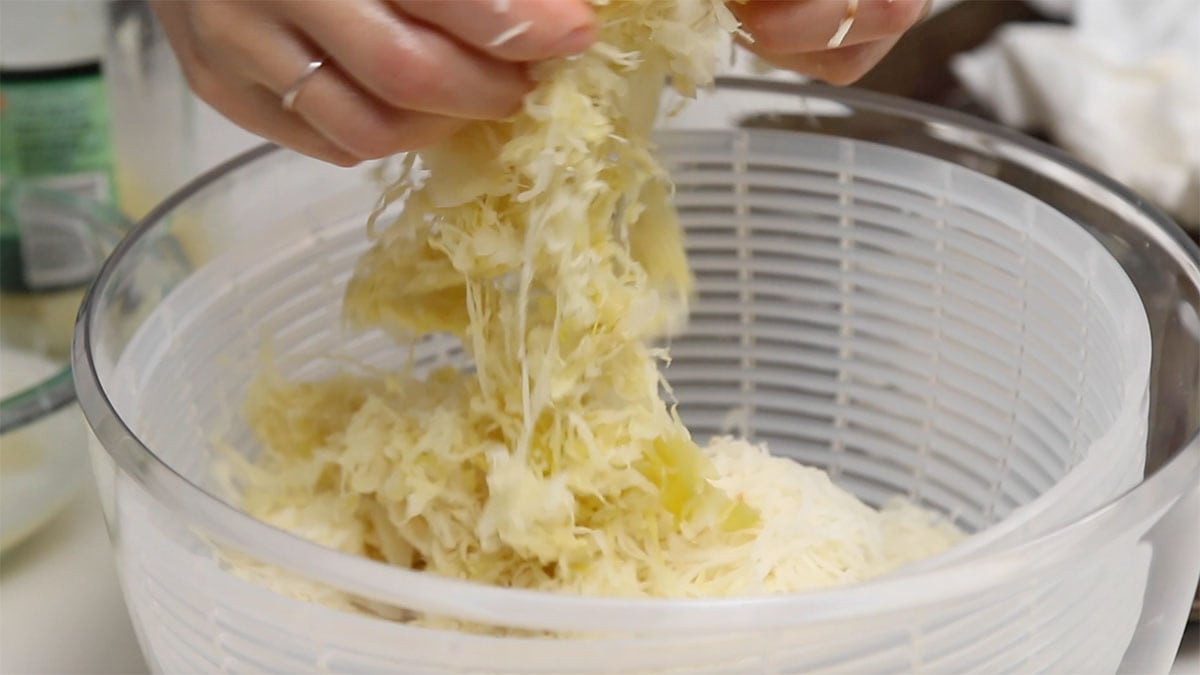 saurekraut being added to a salad spinner already filled with shredded potato