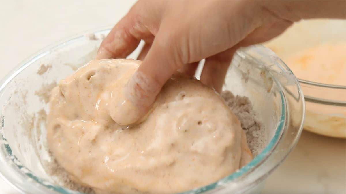 a hand dredging vegan chicken in batter