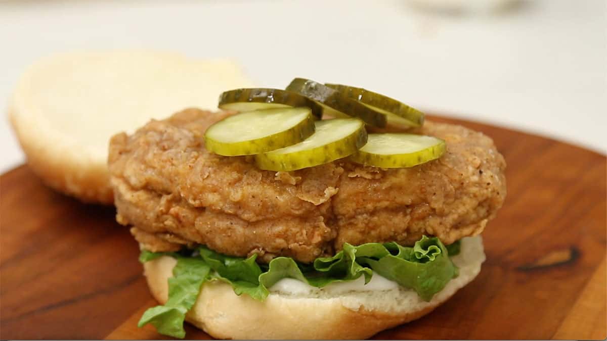 a side view of a vegan fried chicken sandwich assembled with the top bun sitting beside it