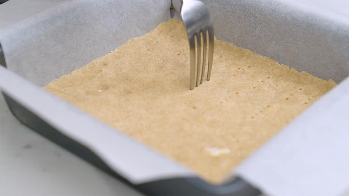 baking pan with shortbread crust pressed into it and a fork poking holes