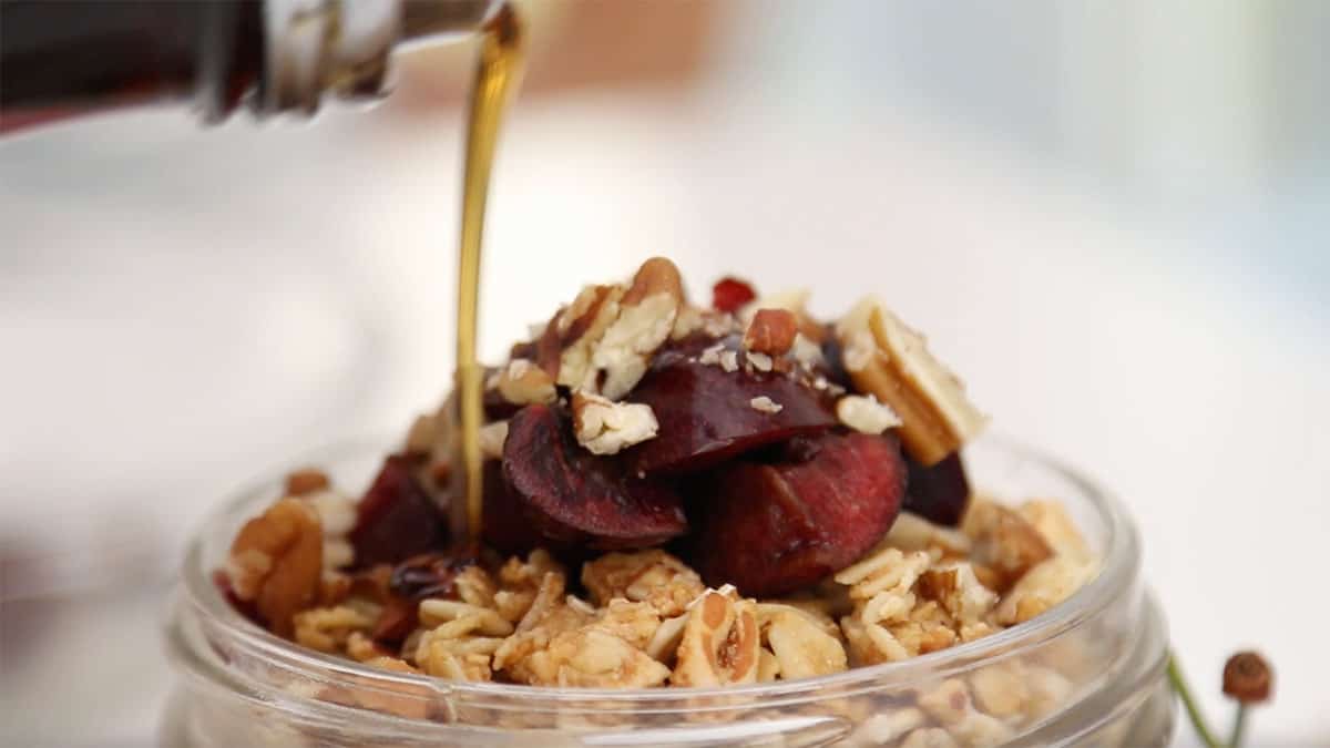 side angle of maple syrup being drizzled on top of cherry pie overnight oats