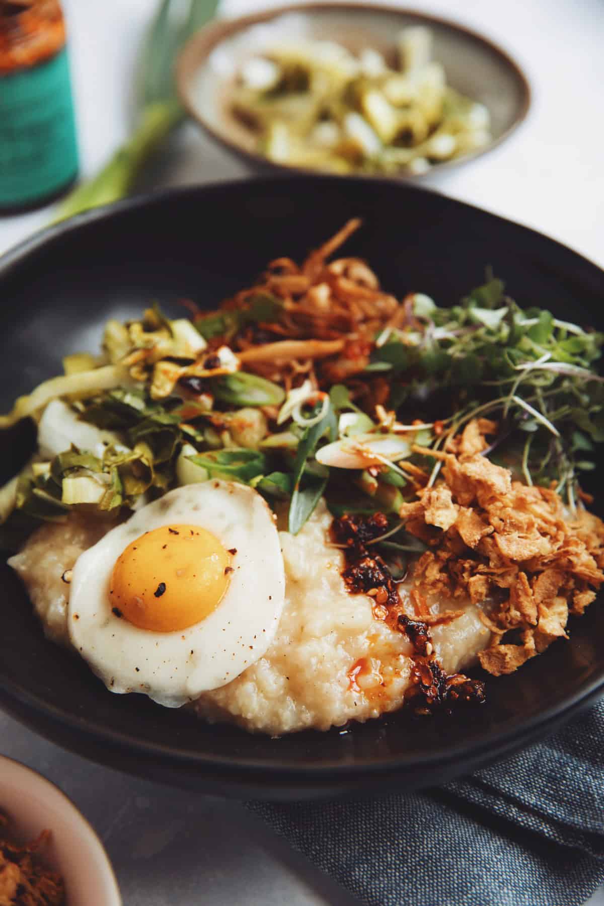 diners view of vegan breakfast congee with colourful toppings in a black bowl on a white background